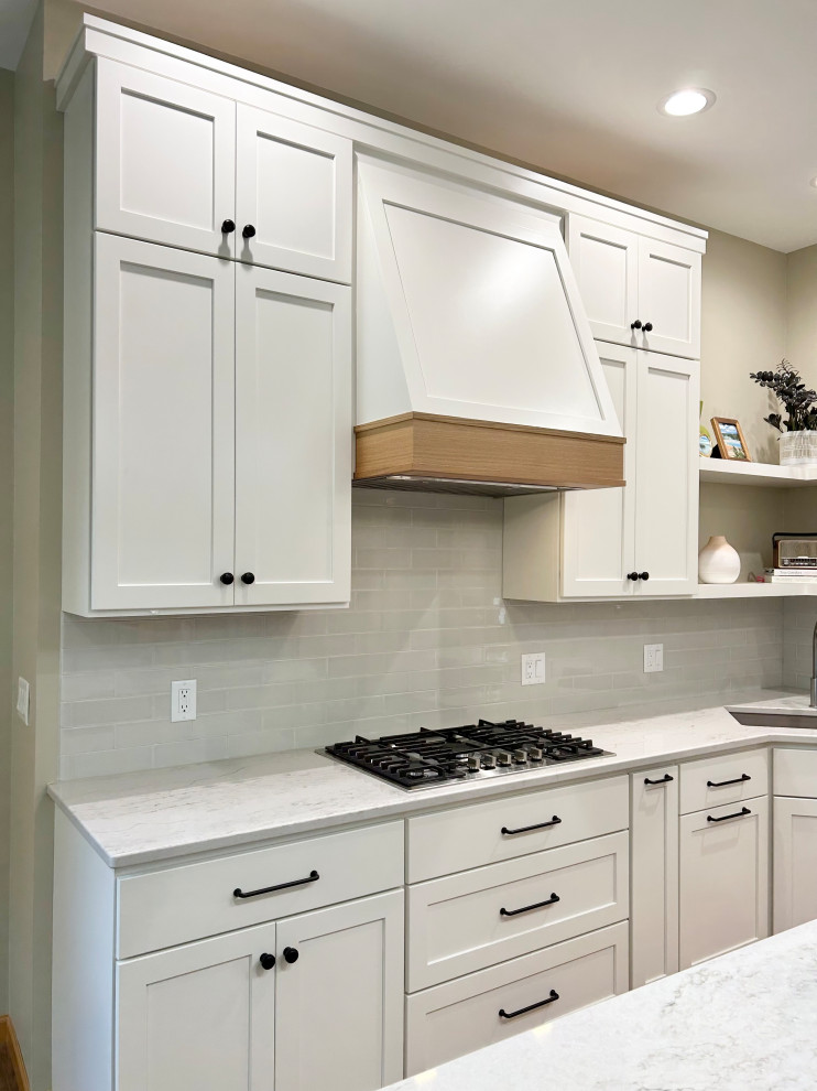 Example of a mid-sized transitional l-shaped medium tone wood floor and brown floor open concept kitchen design with an undermount sink, flat-panel cabinets, white cabinets, quartz countertops, gray backsplash, ceramic backsplash, stainless steel appliances, an island and white countertops