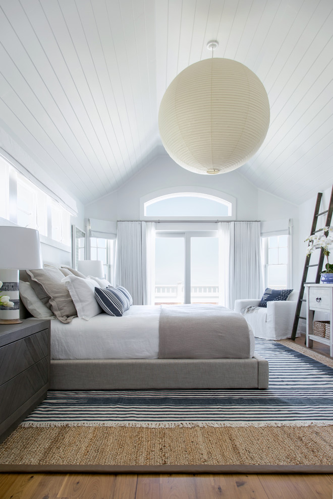 Photo of a large beach style master bedroom in New York with white walls, medium hardwood floors and brown floor.