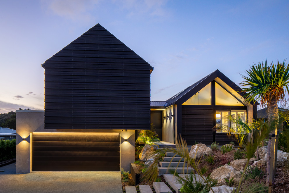 Inspiration pour une grande façade de maison noire design en bois et planches et couvre-joints à niveaux décalés avec un toit en métal et un toit noir.
