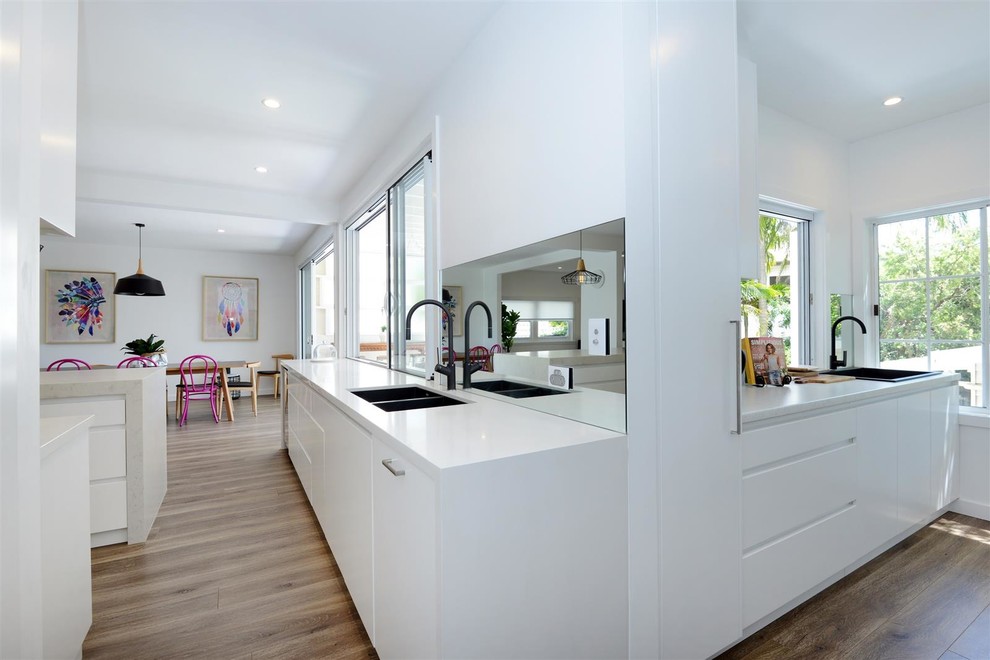 Photo of a beach style l-shaped open plan kitchen in Sydney with white cabinets, with island and white benchtop.