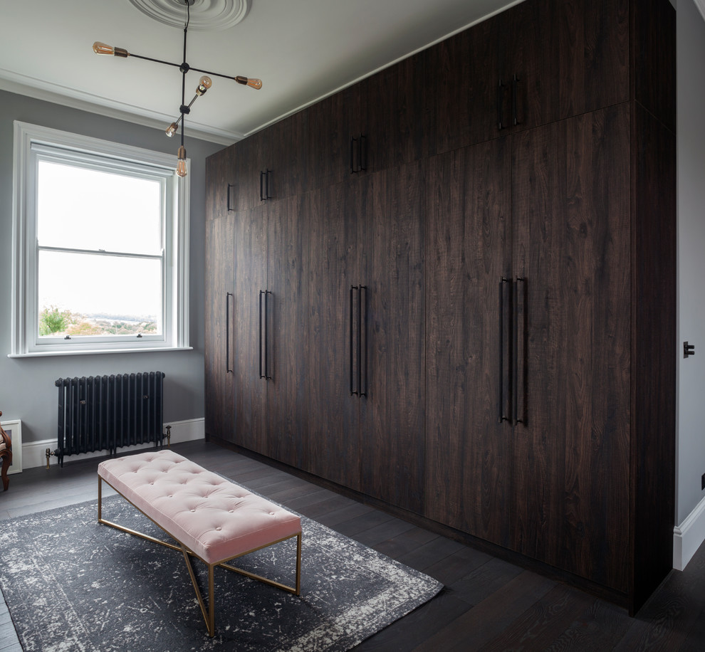 Inspiration for a mid-sized contemporary gender-neutral walk-in wardrobe in London with flat-panel cabinets, dark wood cabinets, dark hardwood floors and brown floor.