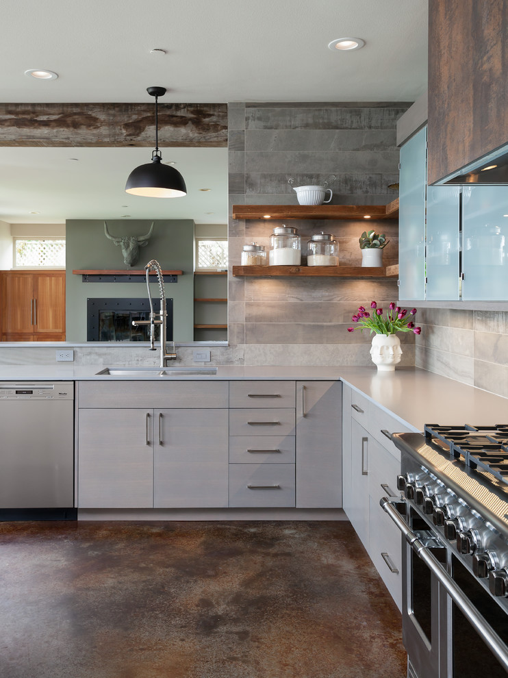 Photo of a mid-sized beach style u-shaped eat-in kitchen in Seattle with a drop-in sink, flat-panel cabinets, grey cabinets, tile benchtops, grey splashback, ceramic splashback, stainless steel appliances, concrete floors, with island and brown floor.