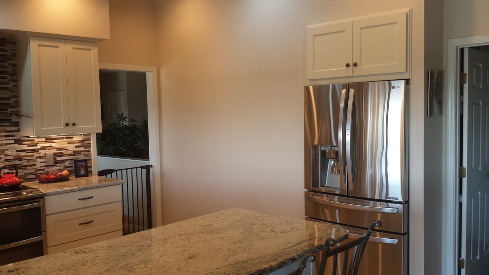 Open concept kitchen - mid-sized transitional u-shaped light wood floor open concept kitchen idea in Phoenix with a single-bowl sink, flat-panel cabinets, white cabinets, granite countertops, brown backsplash, glass tile backsplash, stainless steel appliances and a peninsula