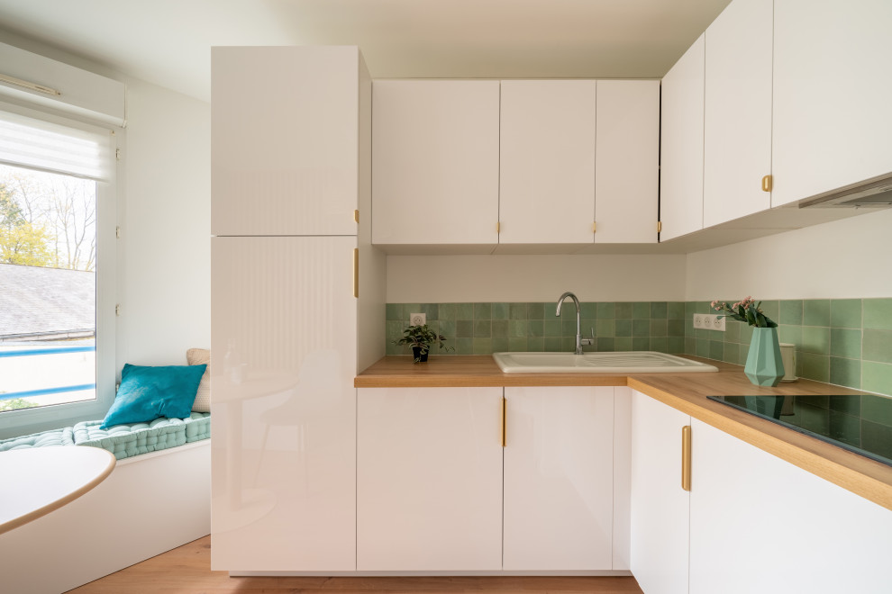 Small contemporary l-shaped open plan kitchen in Nantes with an undermount sink, beaded inset cabinets, white cabinets, wood benchtops, green splashback, porcelain splashback, medium hardwood floors, no island, brown floor and beige benchtop.