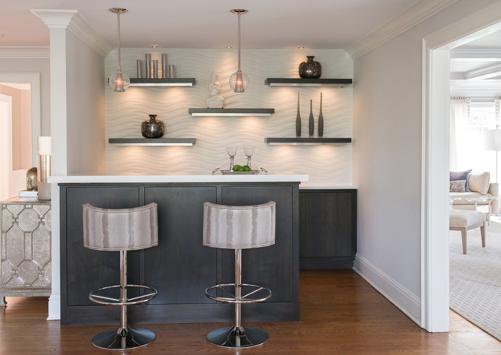 This is an example of a mid-sized transitional u-shaped seated home bar in New York with recessed-panel cabinets, grey cabinets, quartz benchtops, white splashback, medium hardwood floors, brown floor and white benchtop.