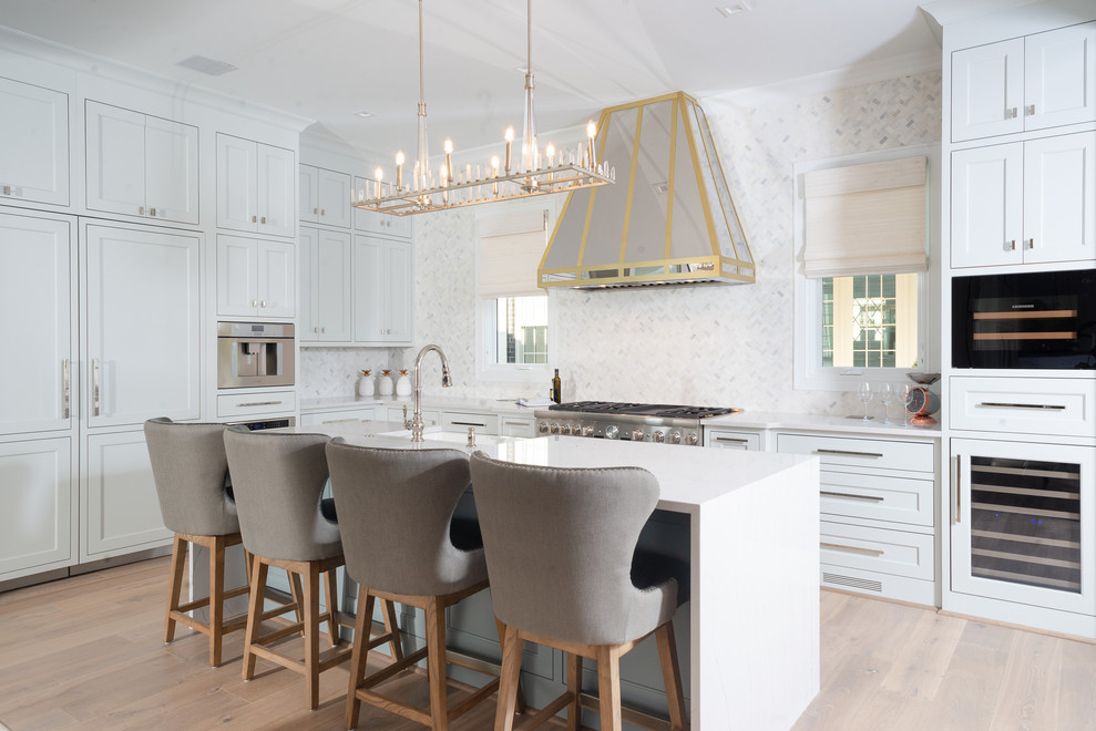 Large transitional l-shaped light wood floor and beige floor eat-in kitchen photo with quartz countertops, an island, white countertops, a farmhouse sink, shaker cabinets, white cabinets, white backsplash and stainless steel appliances