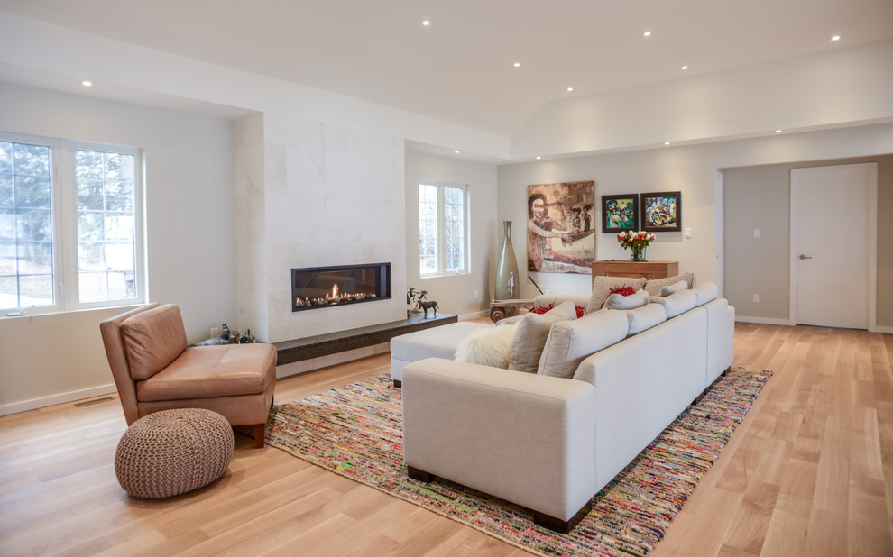 This is an example of a large contemporary family room in Toronto with grey walls, light hardwood floors, a standard fireplace and a stone fireplace surround.