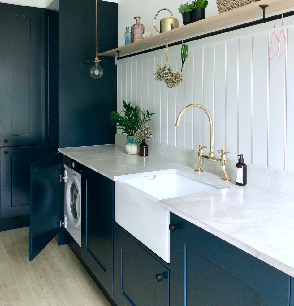 Inspiration for a small traditional single-wall utility room in Other with a farmhouse sink, shaker cabinets, blue cabinets, grey walls, laminate floors, an integrated washer and dryer, beige floor, grey benchtop and planked wall panelling.