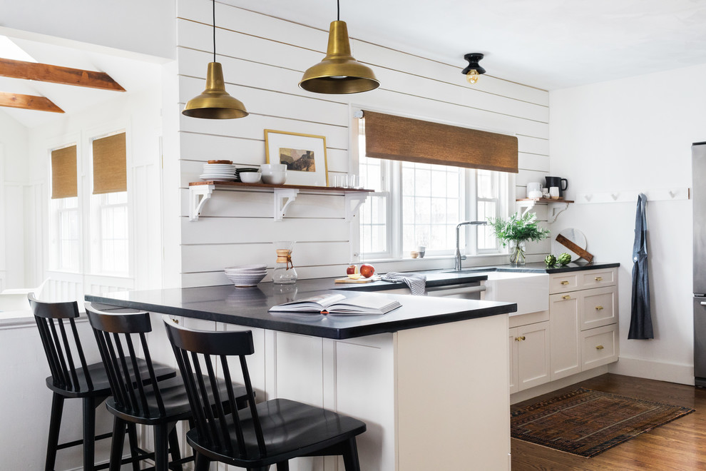 Design ideas for a country kitchen in Boston with a farmhouse sink, white cabinets, white splashback, timber splashback, stainless steel appliances, medium hardwood floors and black benchtop.