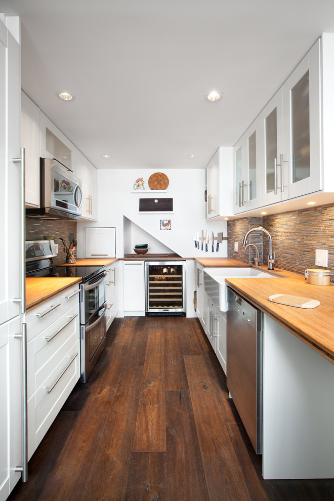Photo of a transitional u-shaped kitchen in Vancouver with a farmhouse sink, shaker cabinets, white cabinets, brown splashback, stainless steel appliances, dark hardwood floors, no island and wood benchtops.