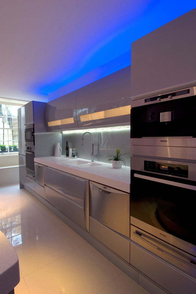 Inspiration for a large modern u-shaped eat-in kitchen in London with an integrated sink, flat-panel cabinets, grey cabinets, solid surface benchtops, glass sheet splashback, porcelain floors, with island, metallic splashback and panelled appliances.