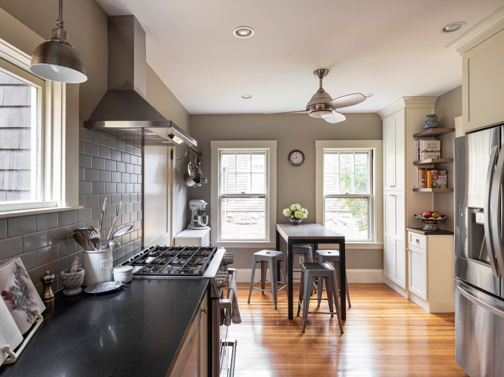 Design ideas for a mid-sized transitional galley kitchen pantry in Boston with a farmhouse sink, shaker cabinets, white cabinets, granite benchtops, grey splashback, subway tile splashback, stainless steel appliances, light hardwood floors, no island and black benchtop.