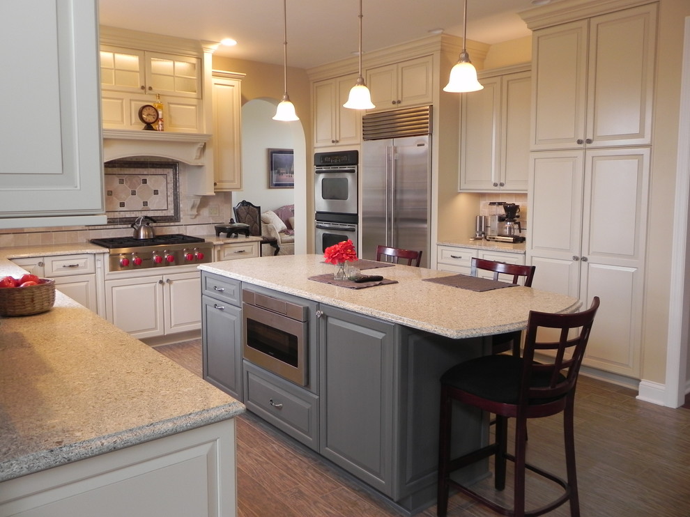 Inspiration for a mid-sized transitional u-shaped light wood floor and brown floor eat-in kitchen remodel with an undermount sink, raised-panel cabinets, white cabinets, granite countertops, beige backsplash, ceramic backsplash, stainless steel appliances and an island