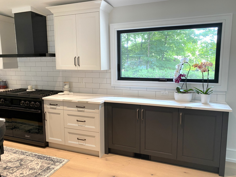 Inspiration for a large transitional l-shaped light wood floor and vaulted ceiling open concept kitchen remodel in Toronto with an undermount sink, recessed-panel cabinets, white cabinets, quartz countertops, white backsplash, porcelain backsplash, stainless steel appliances, an island and white countertops
