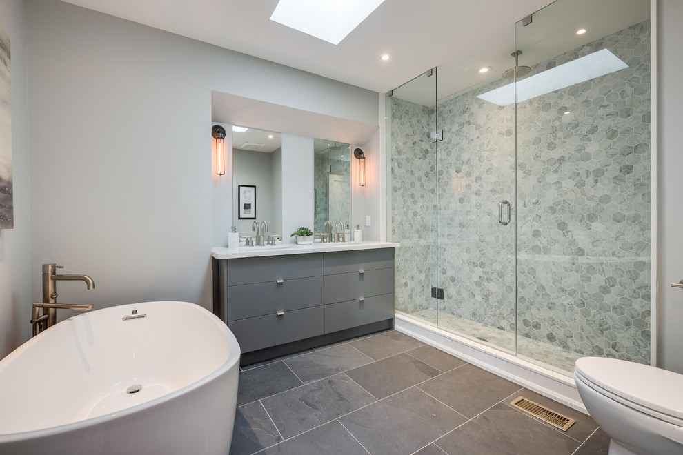 Inspiration for a large contemporary master bathroom in Toronto with flat-panel cabinets, grey cabinets, a freestanding tub, a one-piece toilet, gray tile, porcelain tile, grey walls, porcelain floors, an undermount sink, engineered quartz benchtops, an alcove shower and a hinged shower door.