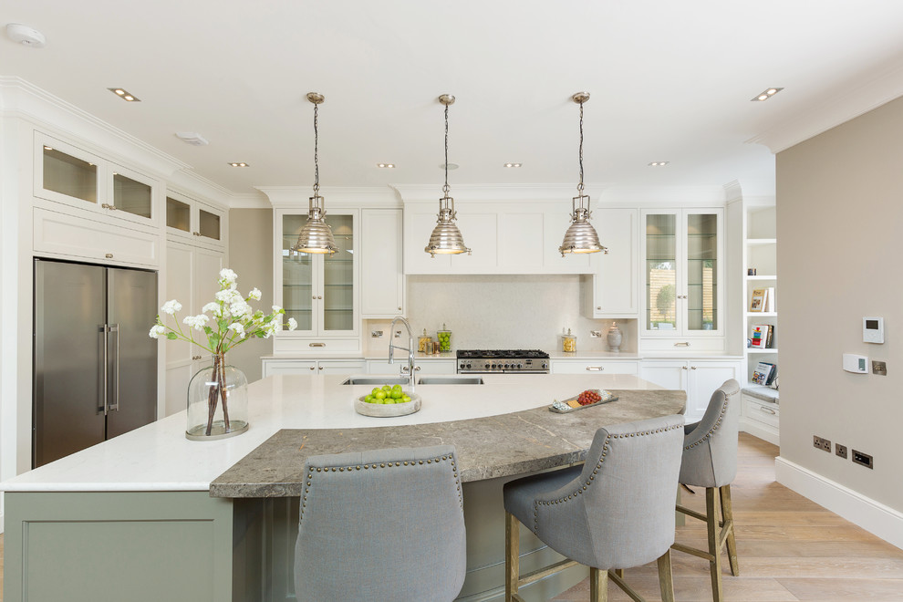 This is an example of a transitional l-shaped eat-in kitchen in Dublin with white splashback, stainless steel appliances, with island, an undermount sink, shaker cabinets, green cabinets, light hardwood floors and beige floor.