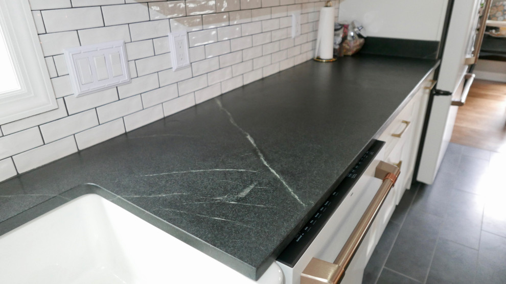 Eat-in kitchen - mid-sized transitional galley porcelain tile and black floor eat-in kitchen idea with a farmhouse sink, shaker cabinets, blue cabinets, marble countertops, white backsplash, subway tile backsplash, white appliances, an island and multicolored countertops