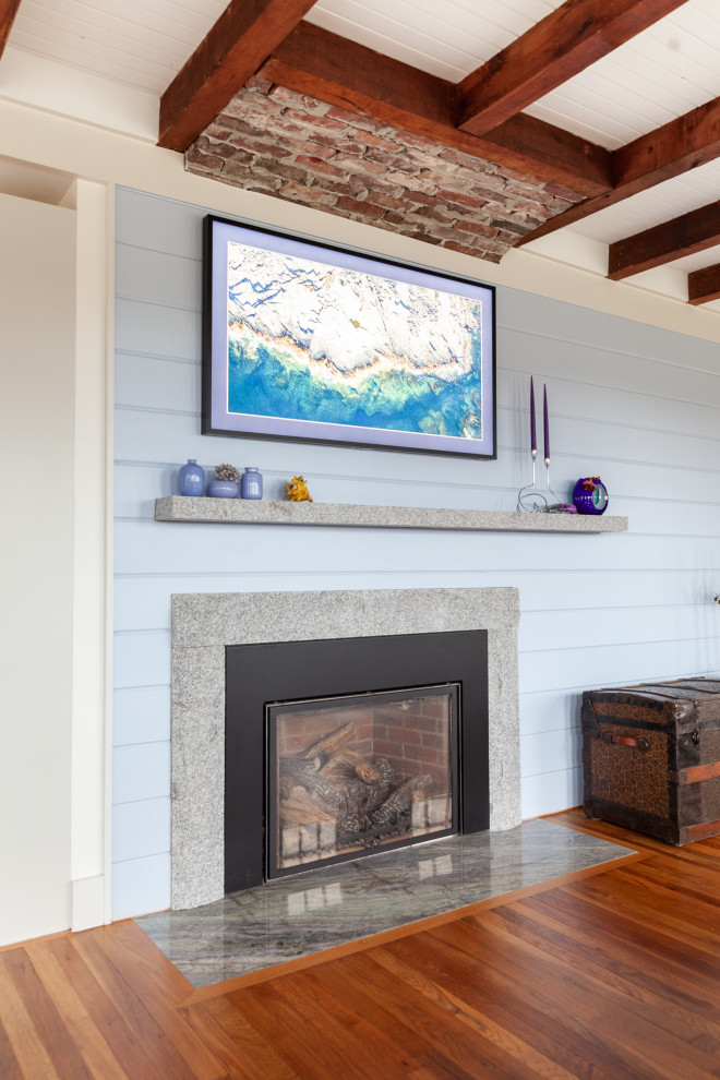 Exemple d'un salon bord de mer de taille moyenne avec un mur bleu, un sol en bois brun, une cheminée standard, un manteau de cheminée en pierre, aucun téléviseur, un sol orange, poutres apparentes et du lambris de bois.