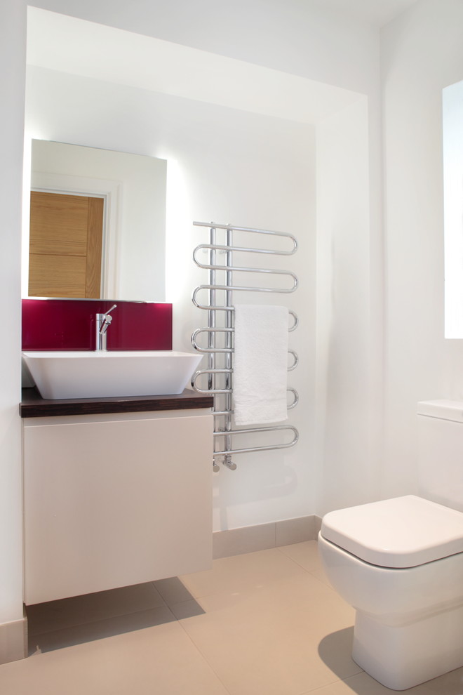 This is an example of a small contemporary kids bathroom in Buckinghamshire with flat-panel cabinets, white cabinets, wood benchtops, a wall-mount toilet, white walls and porcelain floors.