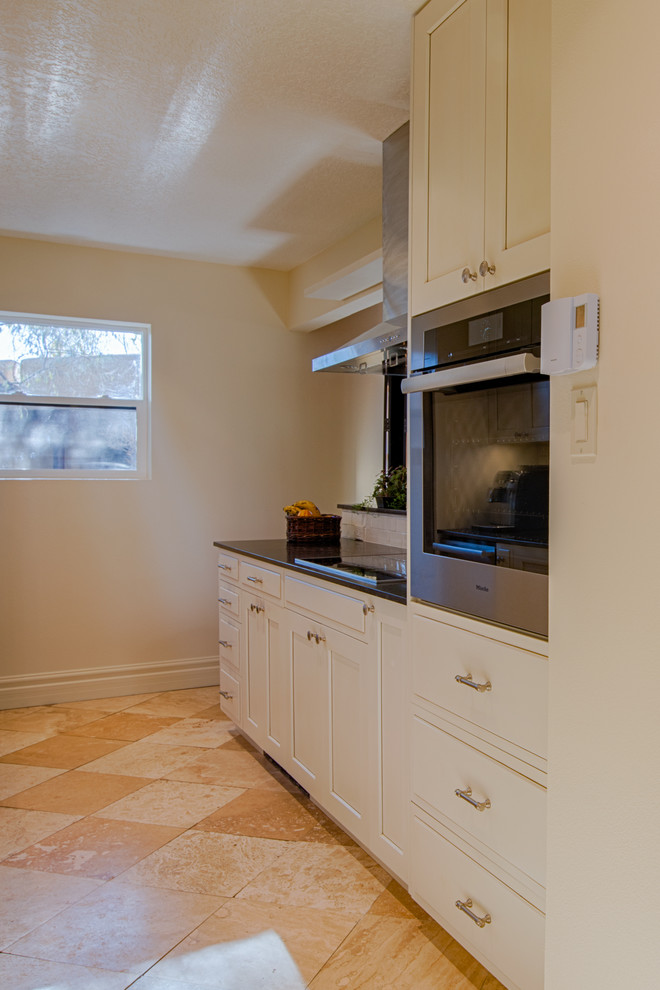 Small transitional galley limestone floor and beige floor open concept kitchen photo in Albuquerque with an undermount sink, shaker cabinets, white cabinets, solid surface countertops, white backsplash, subway tile backsplash, stainless steel appliances and a peninsula