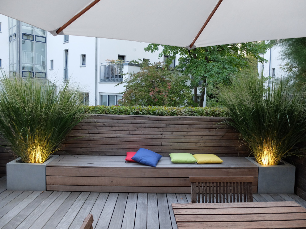This is an example of a small modern side yard partial sun formal garden for summer in Cologne with a container garden, decking and a wood fence.