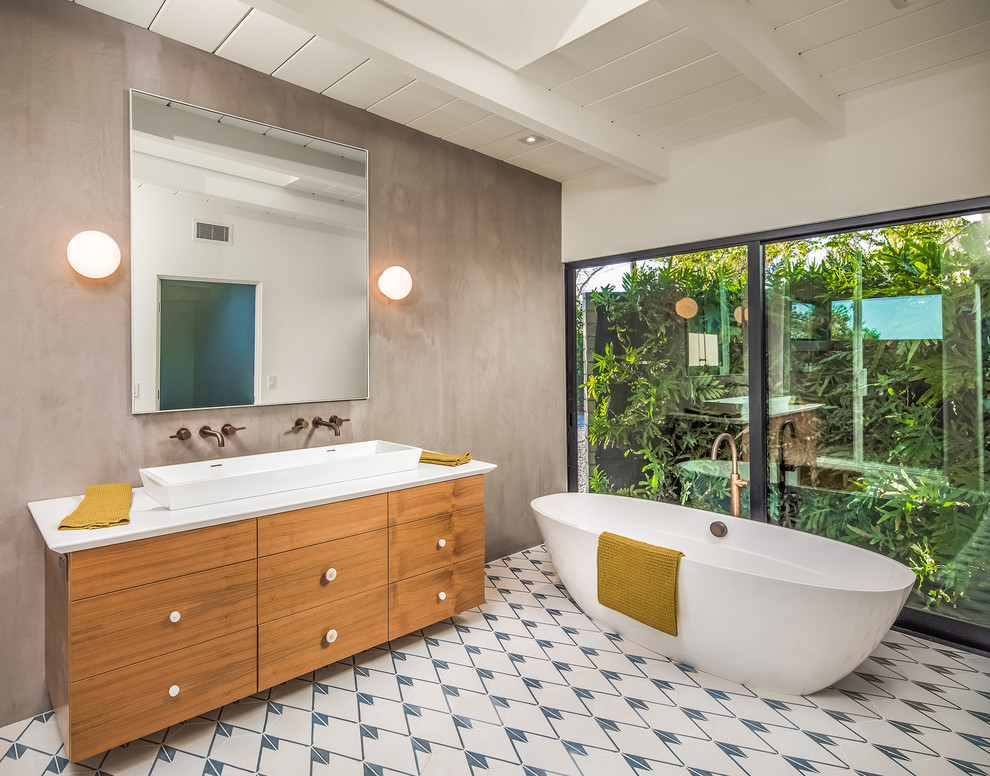Photo of a midcentury master bathroom in San Diego with flat-panel cabinets, medium wood cabinets, a freestanding tub, grey walls, ceramic floors, a vessel sink, white floor and white benchtops.