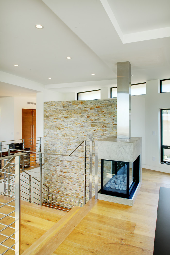 Photo of a mid-sized contemporary loft-style living room in Orange County with white walls, light hardwood floors, a two-sided fireplace, a concrete fireplace surround and a built-in media wall.