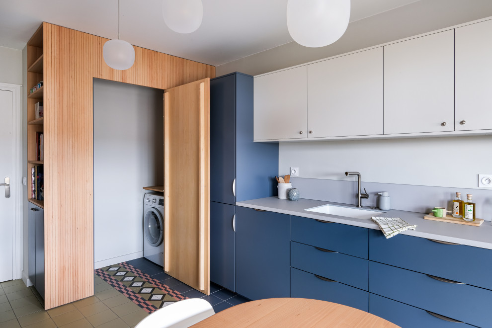 Idée de décoration pour une cuisine linéaire design de taille moyenne avec un placard à porte plane, des portes de placard bleues, carreaux de ciment au sol, un sol multicolore, un plan de travail gris et machine à laver.