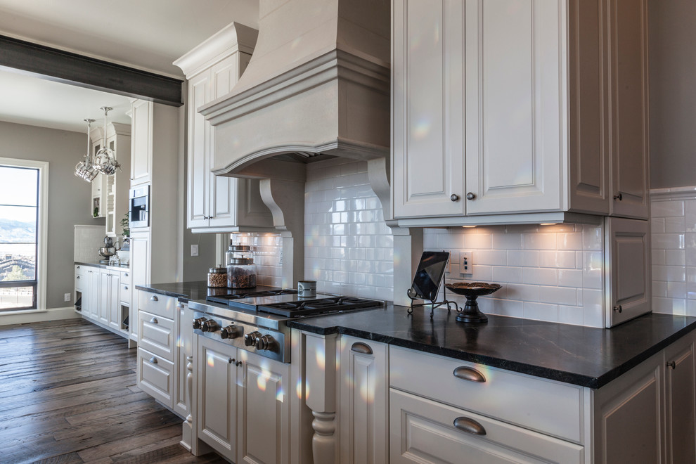 Inspiration for a transitional medium tone wood floor kitchen remodel in Denver with a farmhouse sink, raised-panel cabinets, white cabinets, soapstone countertops, white backsplash, subway tile backsplash, stainless steel appliances and an island