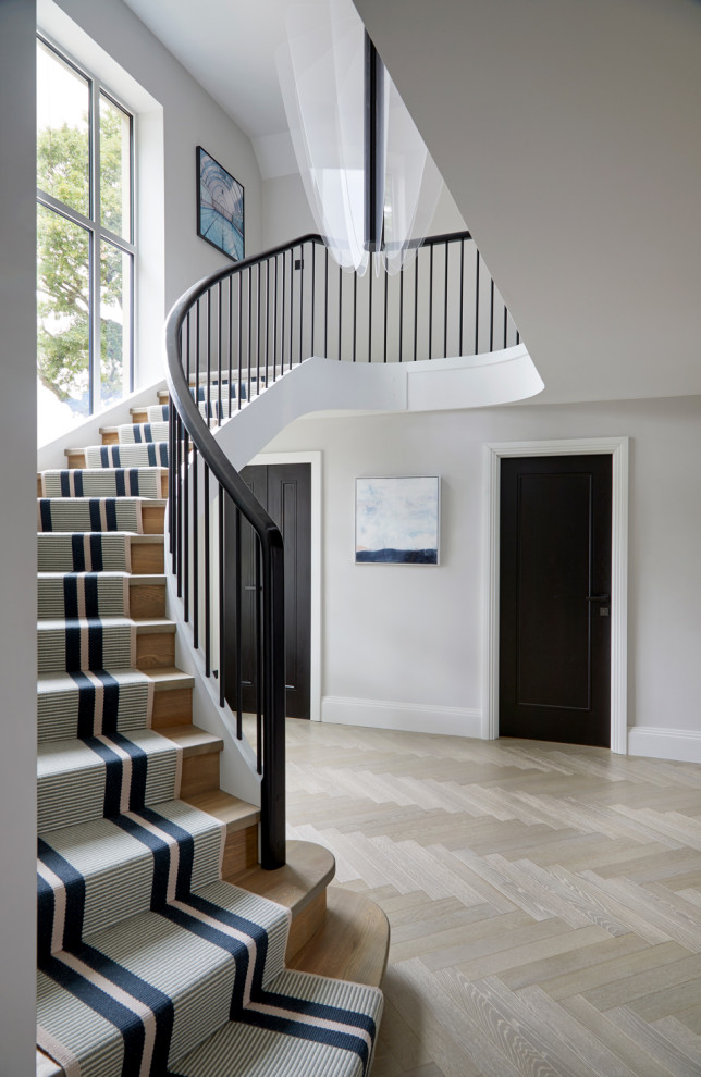 Пример оригинального дизайна: огромная изогнутая деревянная лестница с ступенями с ковровым покрытием, металлическими перилами и обоями на стенах
