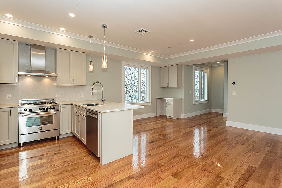 This is an example of a mid-sized modern u-shaped eat-in kitchen in Boston with flat-panel cabinets, white cabinets, granite benchtops, beige splashback, stone slab splashback, stainless steel appliances, medium hardwood floors and a peninsula.