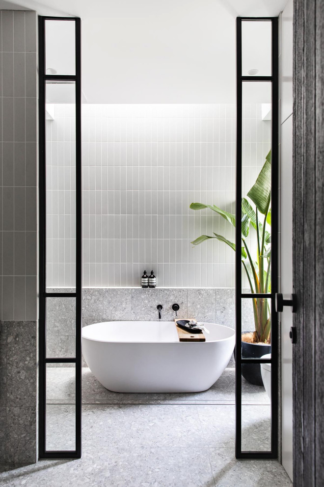 Idéer för industriella badrum, med vita skåp, ett fristående badkar, grå kakel, keramikplattor, grå väggar, klinkergolv i porslin, kaklad bänkskiva och grått golv