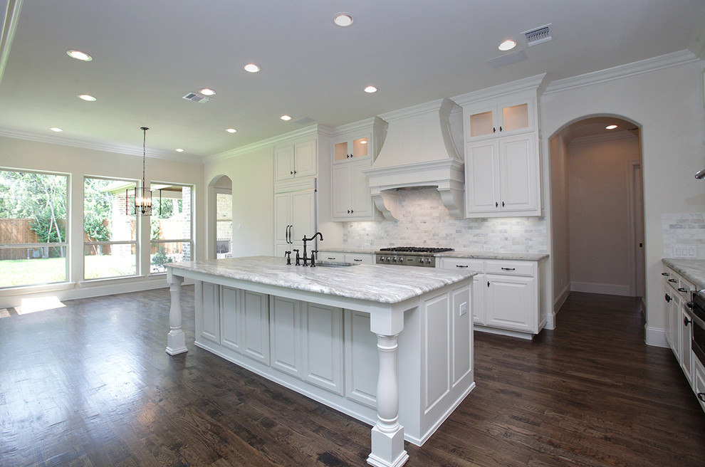 This is an example of a large transitional l-shaped open plan kitchen in Dallas with a single-bowl sink, raised-panel cabinets, white cabinets, granite benchtops, grey splashback, stainless steel appliances, medium hardwood floors and with island.