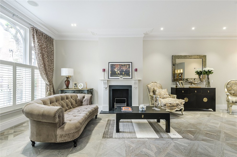 Photo of a mid-sized traditional formal open concept living room in London with beige walls, a standard fireplace, light hardwood floors and no tv.