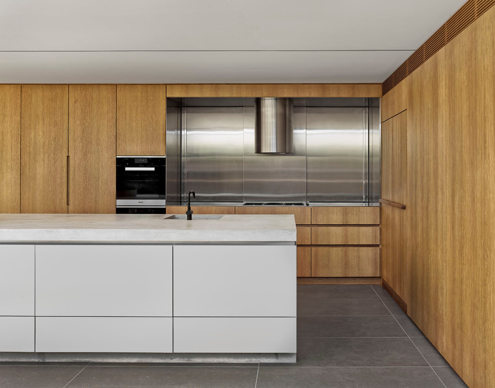 Design ideas for a large modern l-shaped open plan kitchen in Sydney with an integrated sink, flat-panel cabinets, medium wood cabinets, concrete benchtops, metallic splashback, metal splashback, black appliances, ceramic floors and with island.