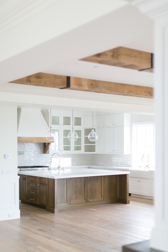 Example of a large transitional u-shaped light wood floor and brown floor open concept kitchen design in Orange County with a farmhouse sink, shaker cabinets, white cabinets, marble countertops, white backsplash, subway tile backsplash, stainless steel appliances and an island
