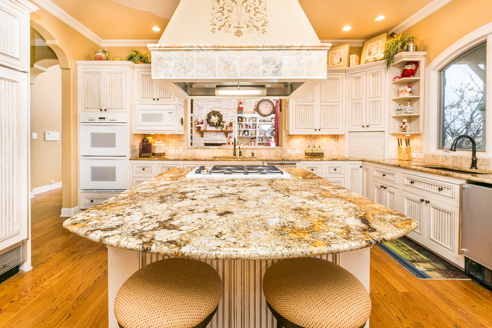 This is an example of a large traditional u-shaped eat-in kitchen in Albuquerque with an undermount sink, louvered cabinets, white cabinets, granite benchtops, beige splashback, stone tile splashback, white appliances, medium hardwood floors and with island.
