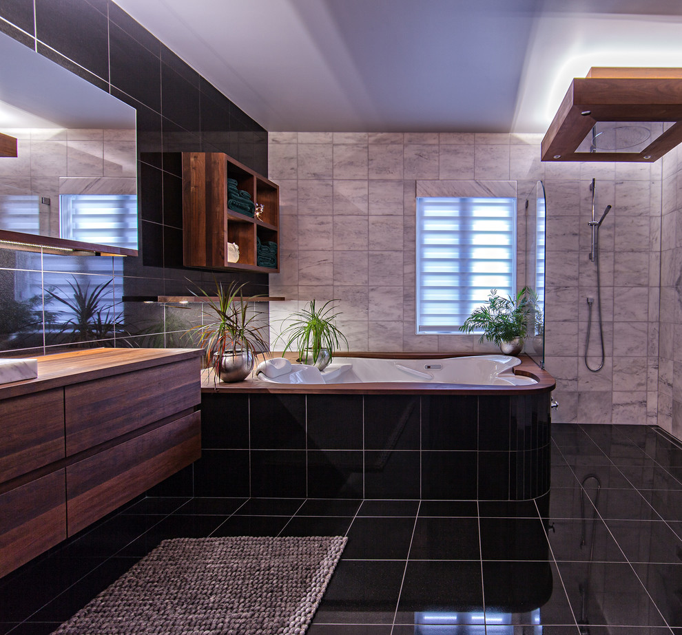 Photo of a mid-sized contemporary master bathroom in Montreal with a drop-in sink, flat-panel cabinets, medium wood cabinets, wood benchtops, an undermount tub, an open shower, a wall-mount toilet, white tile and stone tile.