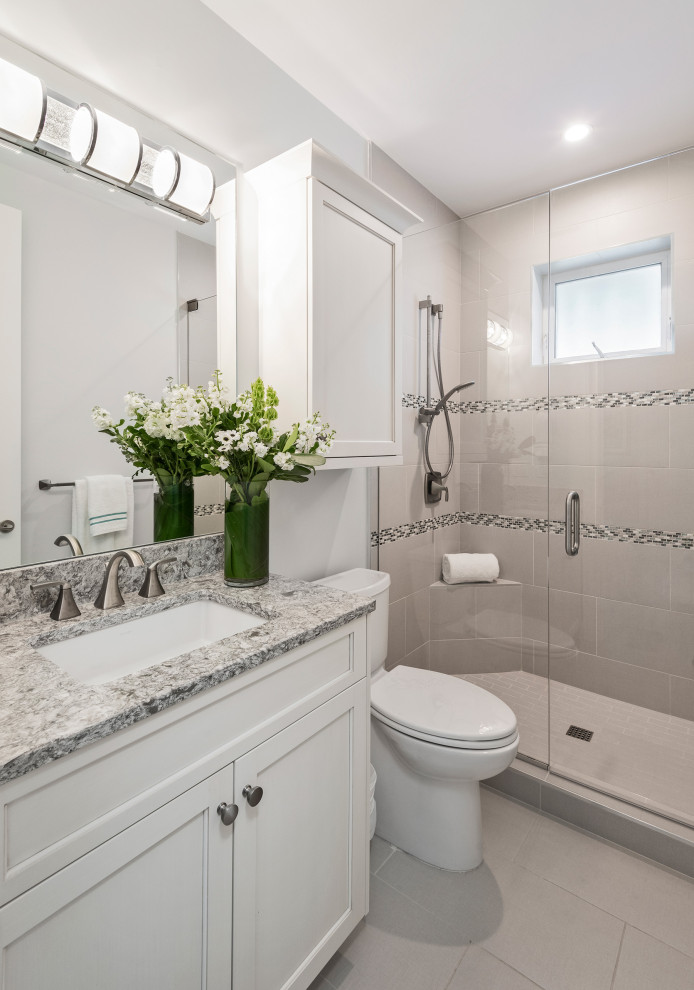 Photo of a beach style 3/4 bathroom in Miami with recessed-panel cabinets, white cabinets, an alcove shower, a two-piece toilet, gray tile, white tile, white walls, an undermount sink, grey floor, a hinged shower door, grey benchtops, a shower seat, a single vanity and a built-in vanity.