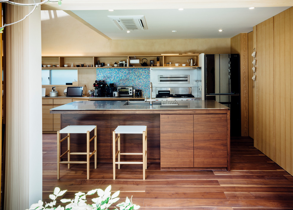 Inspiration for a contemporary galley kitchen in Other with an integrated sink, flat-panel cabinets, medium wood cabinets, stainless steel benchtops, multi-coloured splashback, mosaic tile splashback, black appliances, medium hardwood floors and with island.