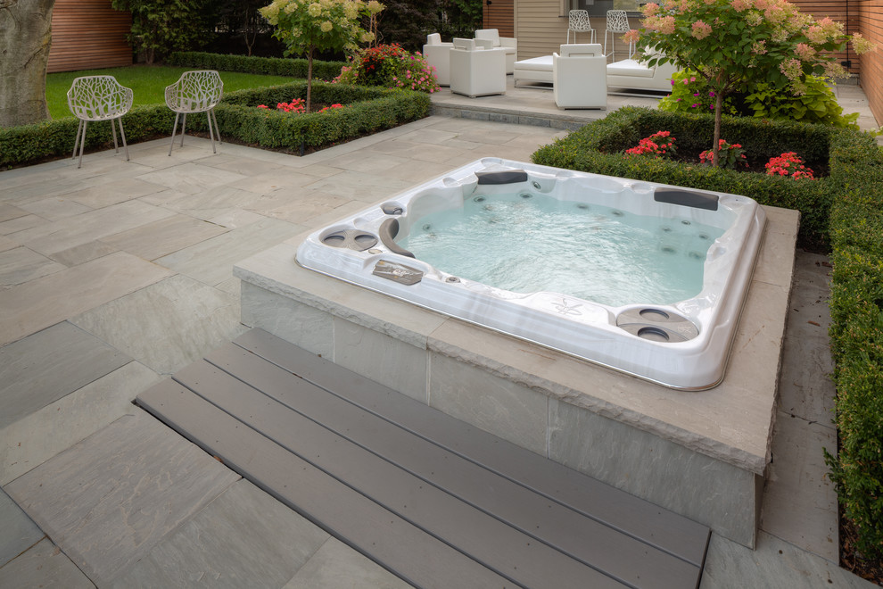 Photo of a large contemporary backyard round lap pool in Toronto with natural stone pavers and a hot tub.