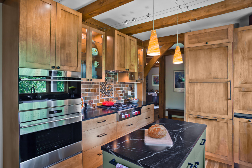 Inspiration for a mid-sized traditional l-shaped separate kitchen in Minneapolis with a farmhouse sink, shaker cabinets, medium wood cabinets, soapstone benchtops, multi-coloured splashback, slate splashback, panelled appliances, light hardwood floors, with island, brown floor and black benchtop.