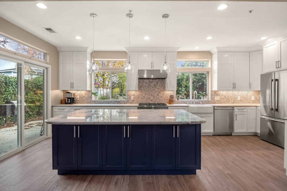 Mid-sized mediterranean open plan kitchen in San Francisco with a farmhouse sink, shaker cabinets, white cabinets, quartzite benchtops, blue splashback, porcelain splashback, stainless steel appliances, porcelain floors, with island, grey floor and blue benchtop.
