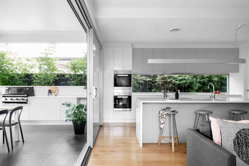 Design ideas for a contemporary galley open plan kitchen in Brisbane with an undermount sink, flat-panel cabinets, medium wood cabinets, window splashback, black appliances, medium hardwood floors, with island and beige floor.