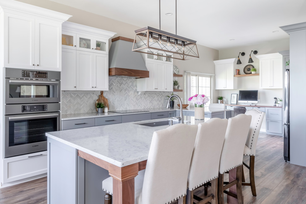 This is an example of a large contemporary l-shaped open plan kitchen in Milwaukee with a double-bowl sink, shaker cabinets, white cabinets, engineered stone countertops, white splashback, marble splashback, stainless steel appliances, vinyl flooring, an island, brown floors and white worktops.