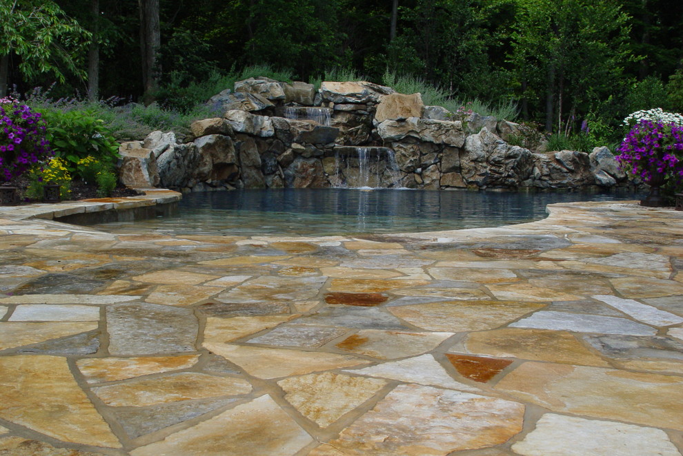 This is an example of a large traditional backyard custom-shaped natural pool in New York with a water feature and natural stone pavers.