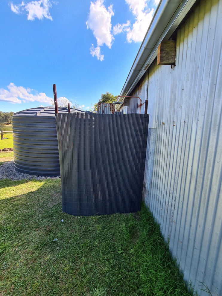 Photo of a mid-sized backyard partial sun garden in Sydney with river rock and a wood fence.