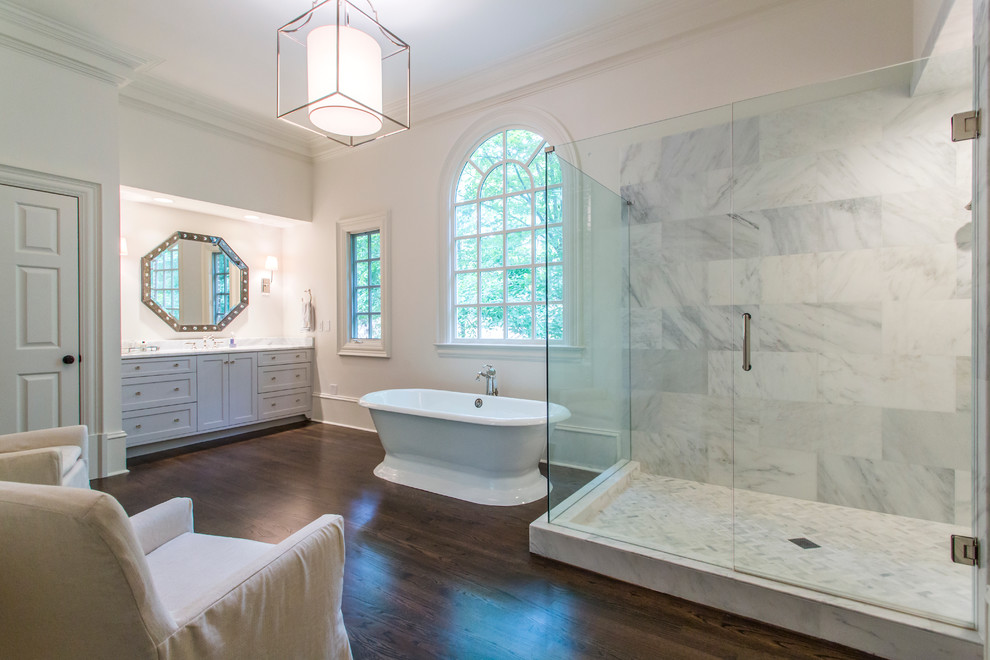 Photo of a transitional master bathroom in Atlanta with shaker cabinets, white cabinets, a freestanding tub, a corner shower, gray tile, white tile, white walls, dark hardwood floors and a hinged shower door.