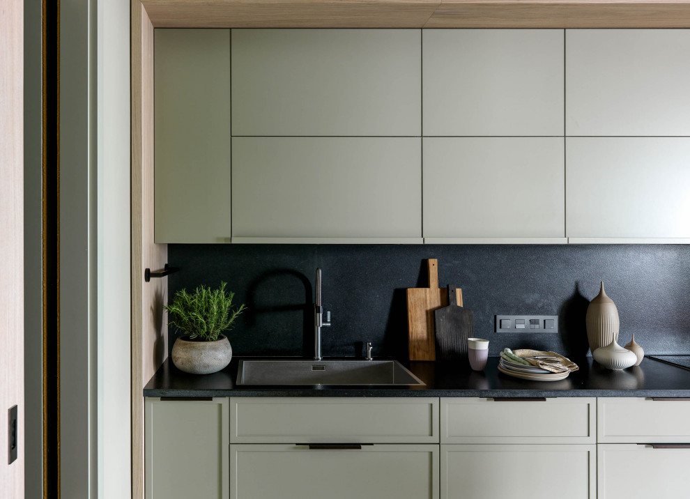 Inspiration for a mid-sized contemporary galley separate kitchen in Moscow with an undermount sink, flat-panel cabinets, green cabinets, granite benchtops, black splashback, stone slab splashback, stainless steel appliances, terrazzo floors, with island, white floor and black benchtop.