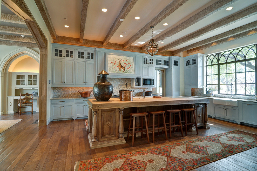 This is an example of a large traditional l-shaped open plan kitchen in Dallas with a farmhouse sink, shaker cabinets, blue cabinets, beige splashback, glass tile splashback, stainless steel appliances, medium hardwood floors, with island and brown floor.